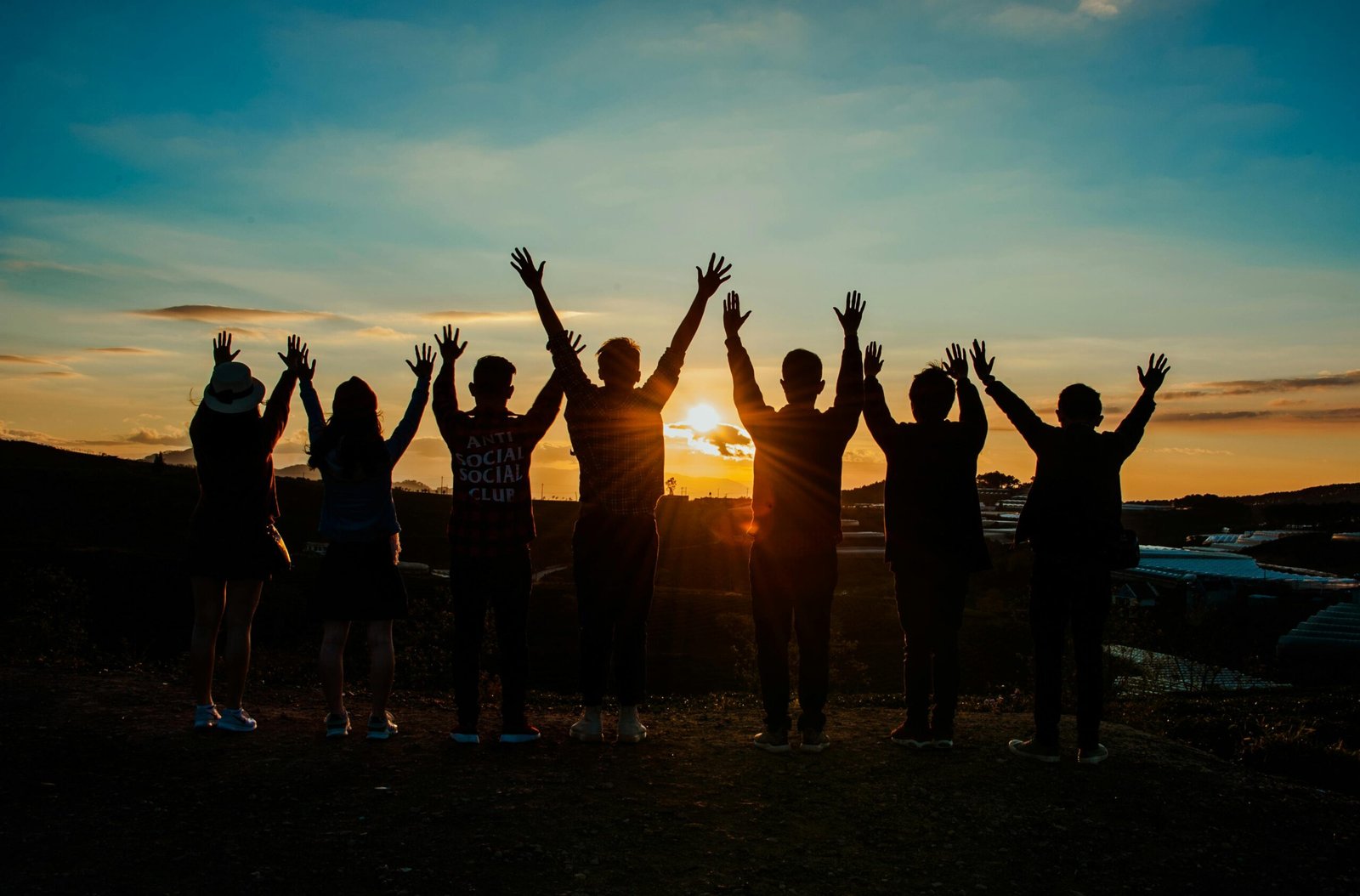 What We Do A diverse group of friends raises their arms in celebration against a vibrant sunset backdrop.